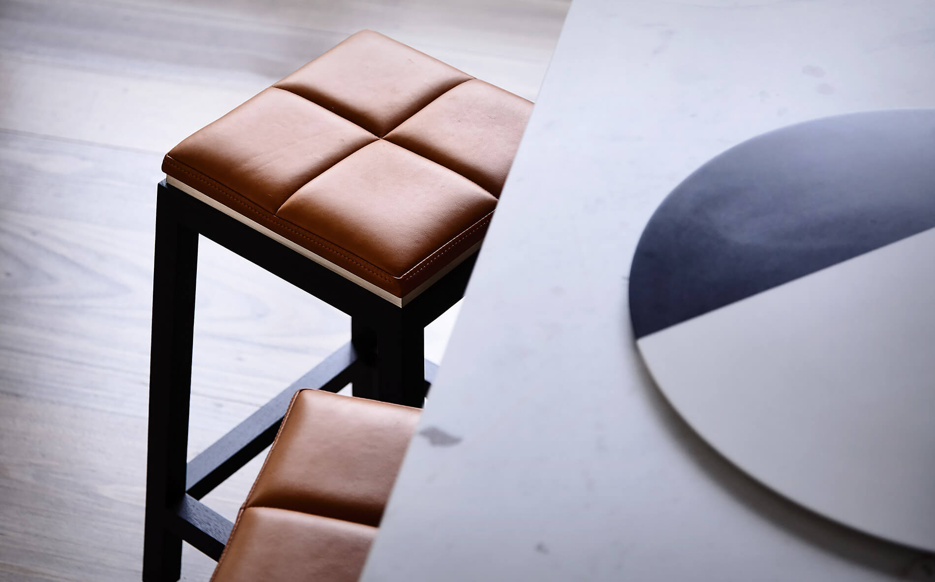 The family island bench slightly overlaps the rich soft tan leather seats of the designer stools included as a feature in this family home by Australian designer Francocrea