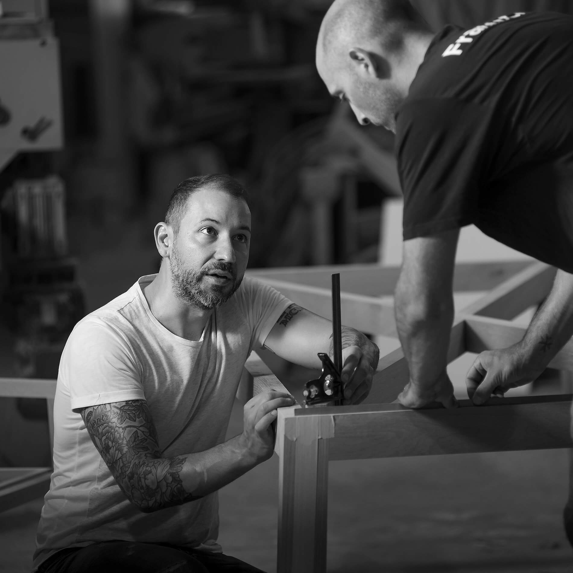 Furniture designer Franco Crea crouching next to his solid wood table measuring the table in his Adelaide workshop