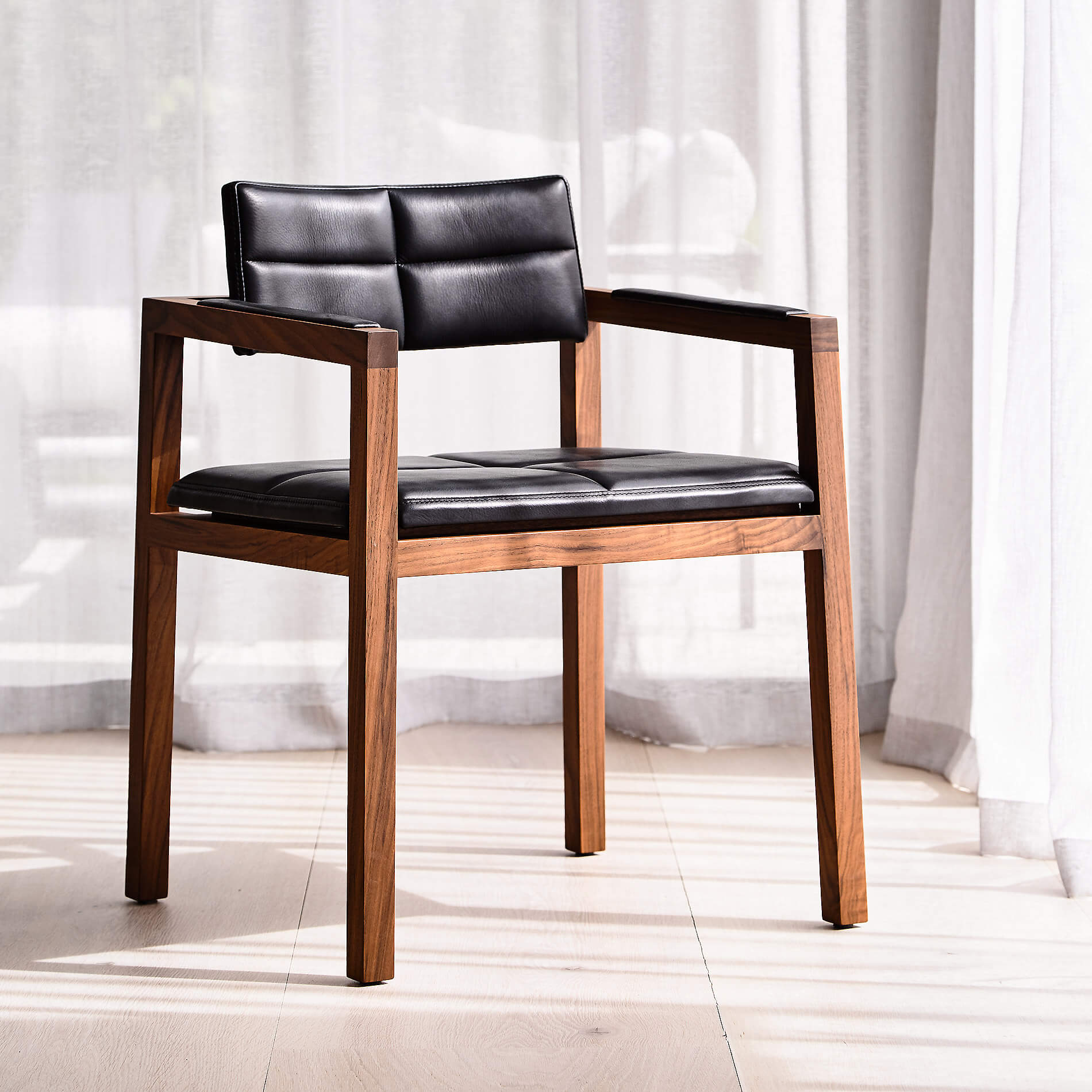 sun shines in from full height glass windows onto designer dining chair with a walnut frame and soft supple black leather